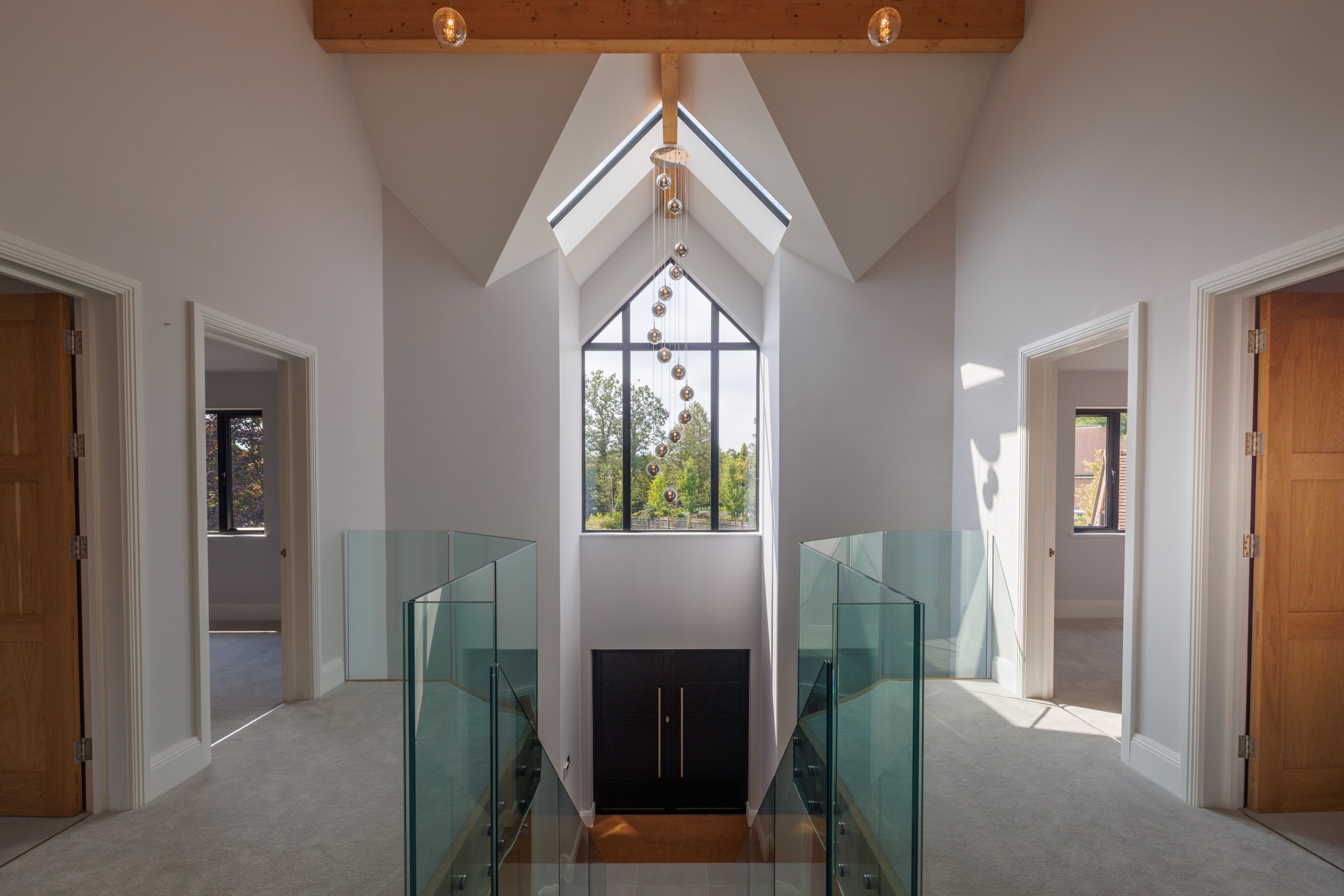 Vaulted galleried landing with glass balustrades, exposed oak beams and a tall glazed gable